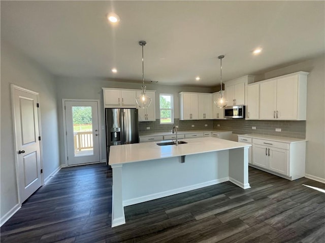 kitchen featuring appliances with stainless steel finishes, decorative light fixtures, white cabinetry, sink, and a kitchen island with sink