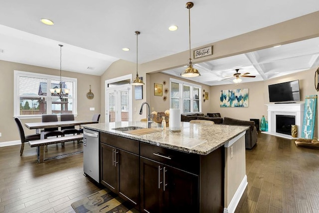 kitchen with light stone counters, sink, hanging light fixtures, and a center island with sink