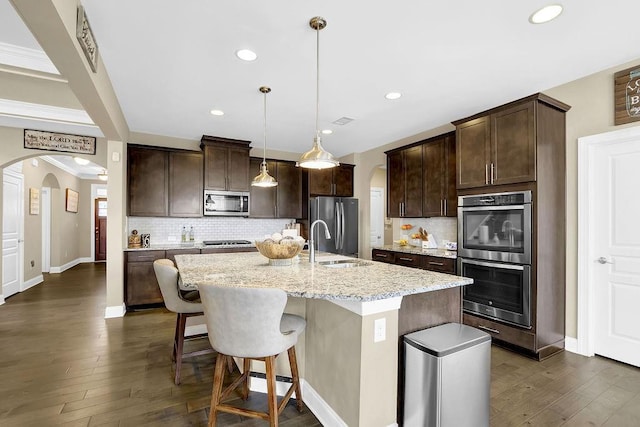 kitchen with decorative light fixtures, an island with sink, sink, dark brown cabinetry, and stainless steel appliances