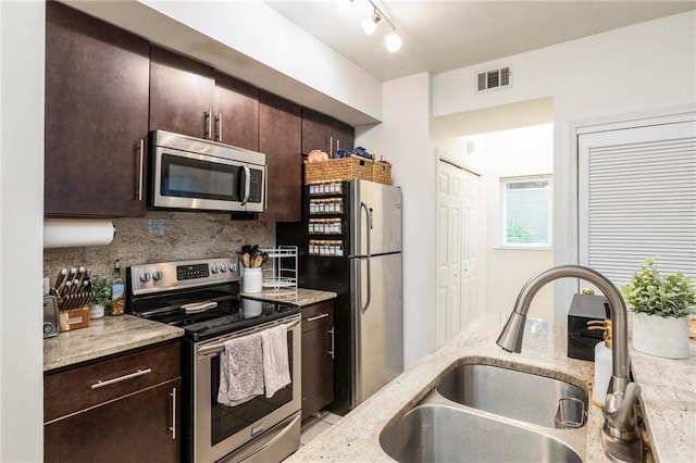 kitchen with light stone countertops, appliances with stainless steel finishes, dark brown cabinets, and sink