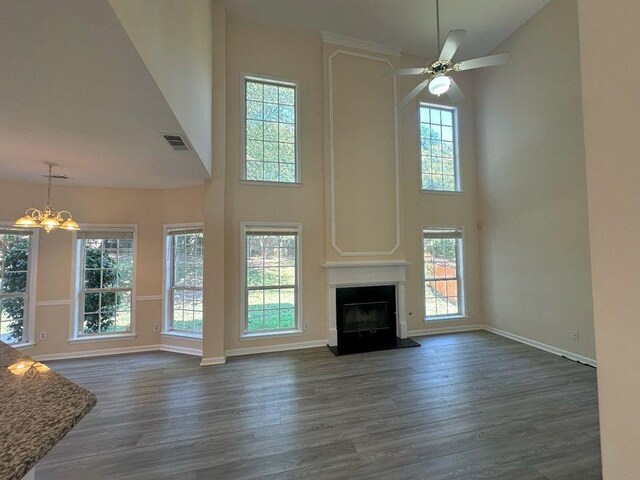 unfurnished living room featuring dark hardwood / wood-style flooring, a wealth of natural light, ceiling fan with notable chandelier, and a high ceiling