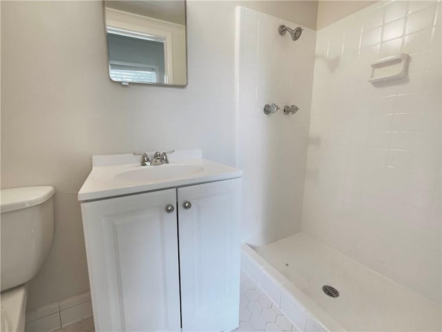 bathroom featuring vanity, toilet, tiled shower, and tile patterned flooring