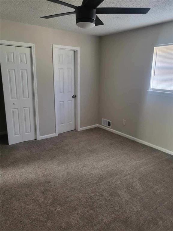 unfurnished bedroom featuring a textured ceiling, carpet, ceiling fan, and two closets