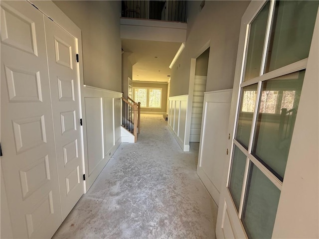 hall with wainscoting, a decorative wall, and unfinished concrete floors