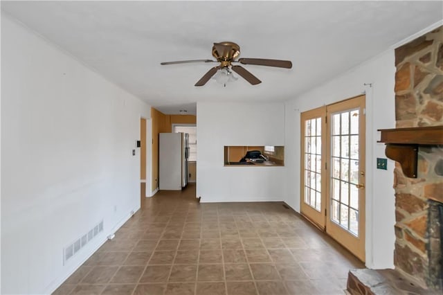 unfurnished room with ceiling fan, visible vents, and a stone fireplace