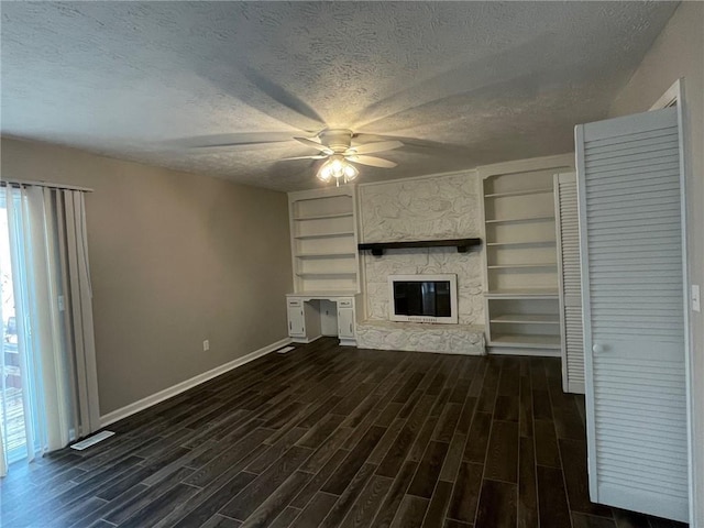 unfurnished living room with a textured ceiling, ceiling fan, dark wood-style flooring, a fireplace, and baseboards