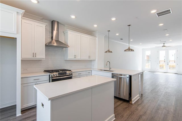 kitchen with wall chimney range hood, white cabinetry, sink, pendant lighting, and stainless steel appliances