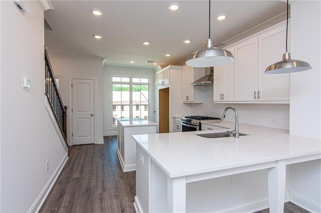 kitchen with dark hardwood / wood-style flooring, kitchen peninsula, wall chimney exhaust hood, decorative light fixtures, and stainless steel gas range