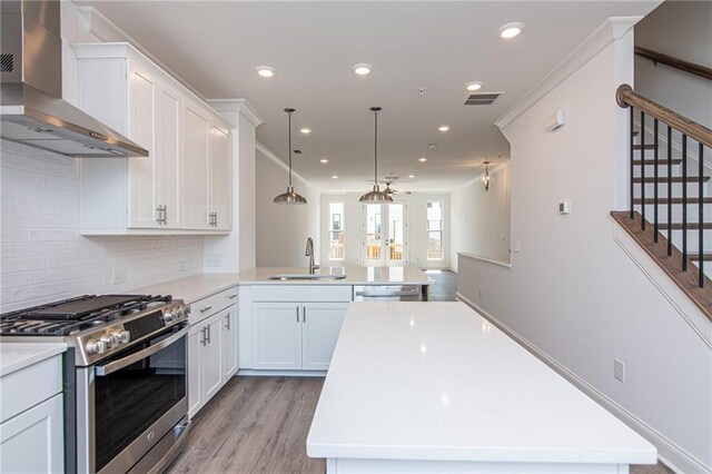 kitchen with wall chimney range hood, white cabinetry, light hardwood / wood-style flooring, sink, and stainless steel appliances