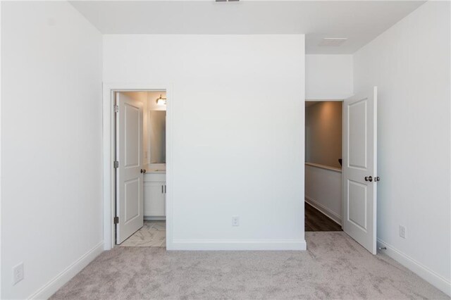 unfurnished bedroom with ensuite bathroom and light colored carpet