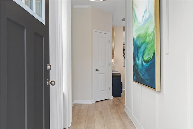 corridor with light wood-style flooring, ornamental molding, and baseboards