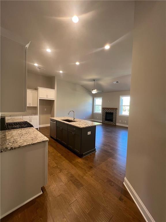 kitchen featuring dark hardwood / wood-style floors, white cabinetry, an island with sink, sink, and light stone counters