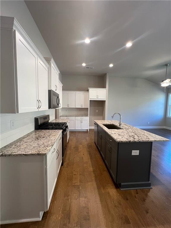 kitchen featuring sink, appliances with stainless steel finishes, a kitchen island with sink, light stone countertops, and white cabinets