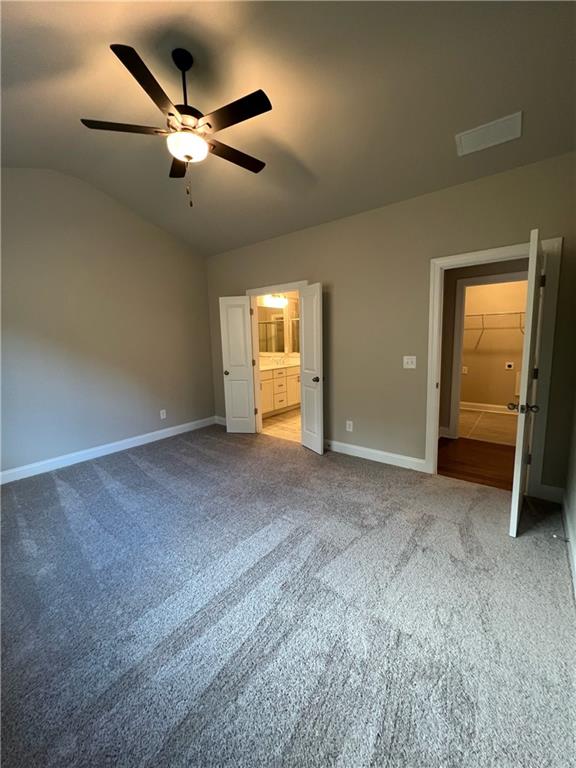 unfurnished bedroom featuring ceiling fan, lofted ceiling, carpet floors, and ensuite bath