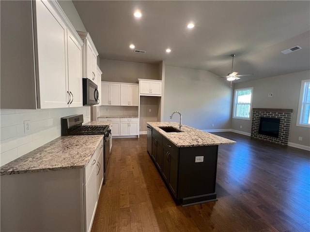 kitchen with sink, stainless steel gas range oven, a center island with sink, a fireplace, and light stone countertops