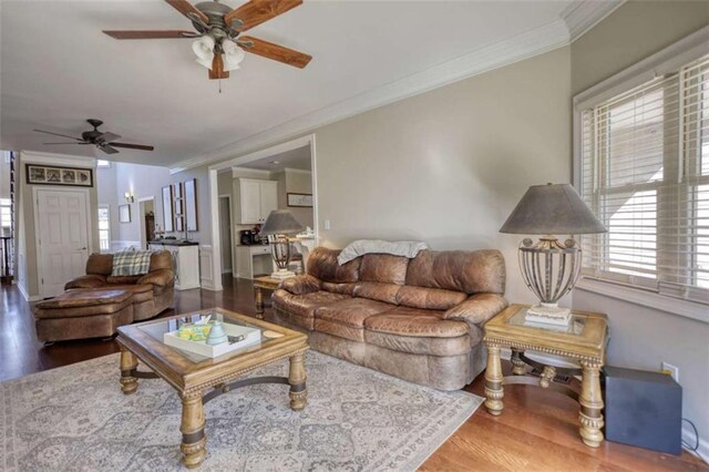 living area with baseboards, crown molding, wood finished floors, and a ceiling fan