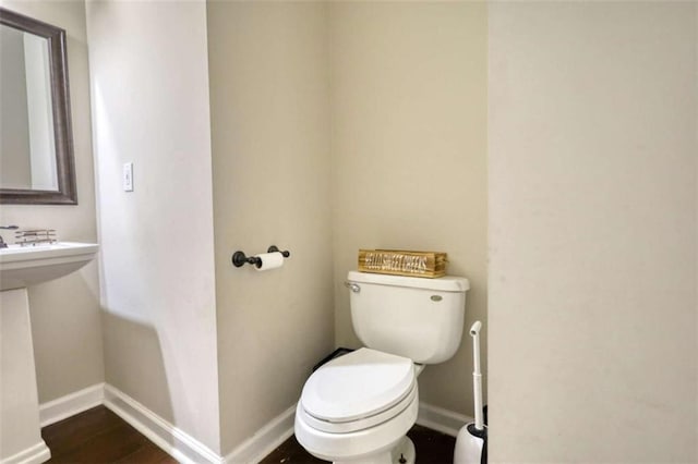 bathroom featuring baseboards, wood finished floors, and toilet