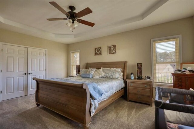 bedroom with a tray ceiling, ceiling fan, a closet, and carpet floors
