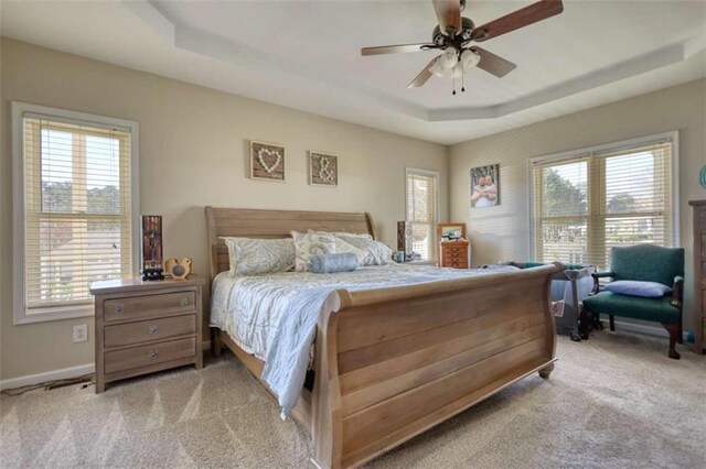 bedroom with a tray ceiling, baseboards, light carpet, and a ceiling fan