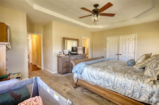bedroom featuring a closet, carpet flooring, a ceiling fan, a raised ceiling, and baseboards