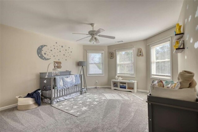 carpeted bedroom featuring baseboards, a crib, and a ceiling fan