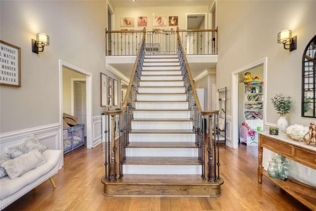 staircase featuring wainscoting, wood finished floors, and a towering ceiling