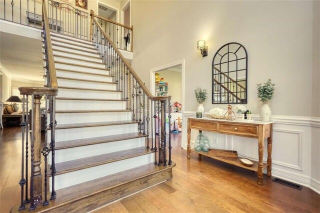 stairs featuring a wainscoted wall, a decorative wall, visible vents, wood finished floors, and a high ceiling