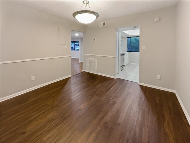 empty room featuring plenty of natural light, wood finished floors, visible vents, and baseboards