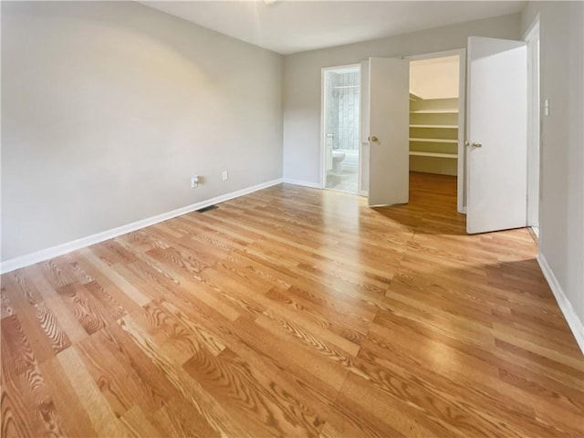 unfurnished bedroom with light wood-type flooring, ensuite bath, baseboards, and a walk in closet