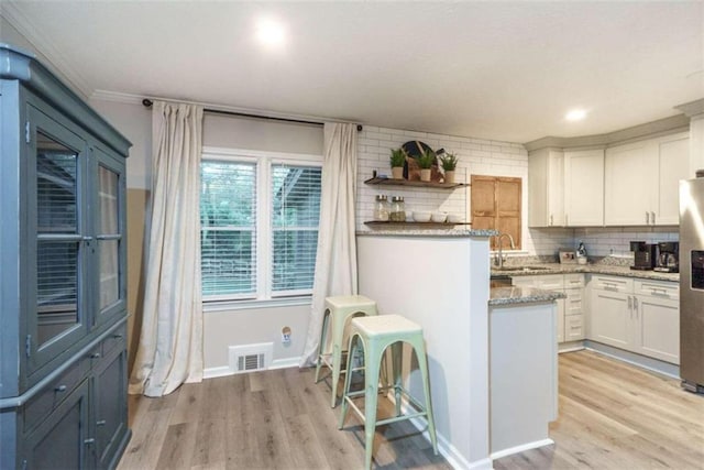 kitchen featuring white cabinetry, sink, stainless steel refrigerator with ice dispenser, light hardwood / wood-style floors, and decorative backsplash