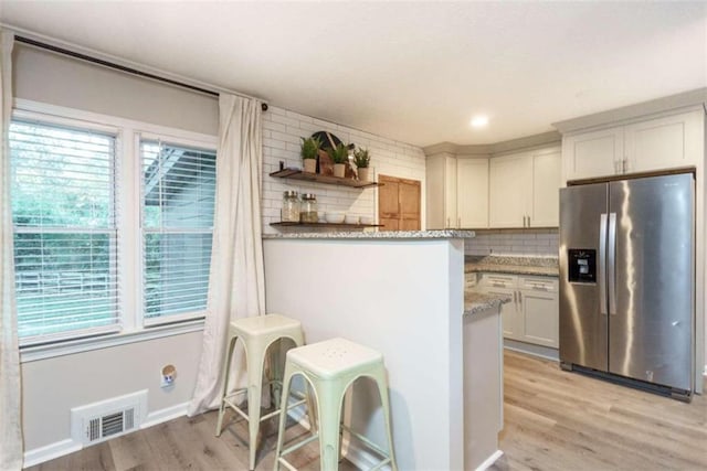 kitchen featuring white cabinetry, stainless steel fridge with ice dispenser, plenty of natural light, dark stone counters, and decorative backsplash