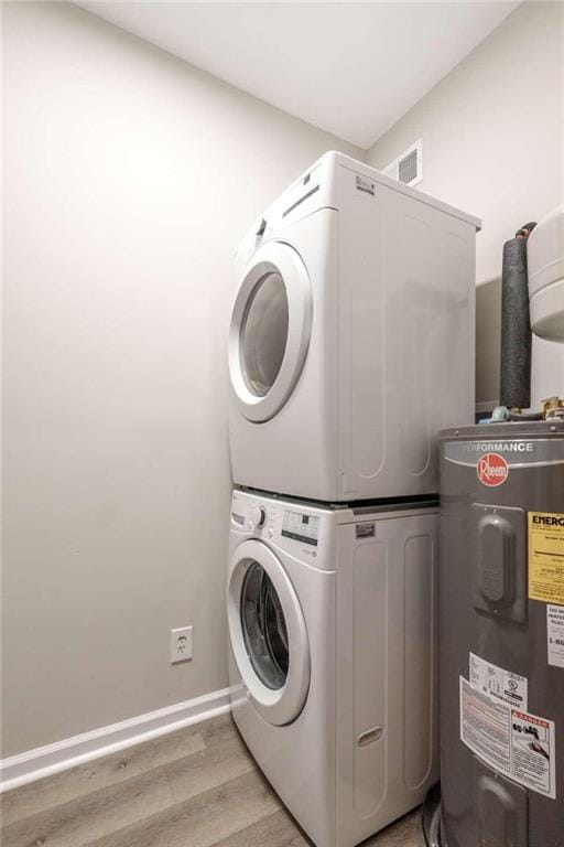 laundry area with stacked washer / dryer, electric water heater, and light wood-type flooring