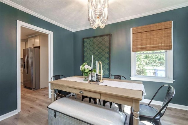 dining room featuring light hardwood / wood-style flooring, ornamental molding, a textured ceiling, and an inviting chandelier