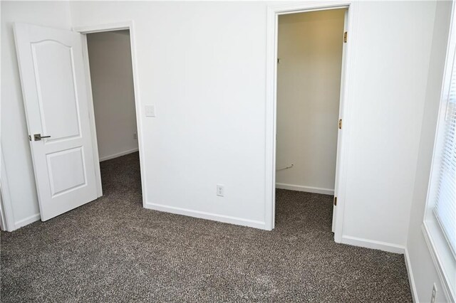 unfurnished bedroom with dark carpet, a spacious closet, and a closet