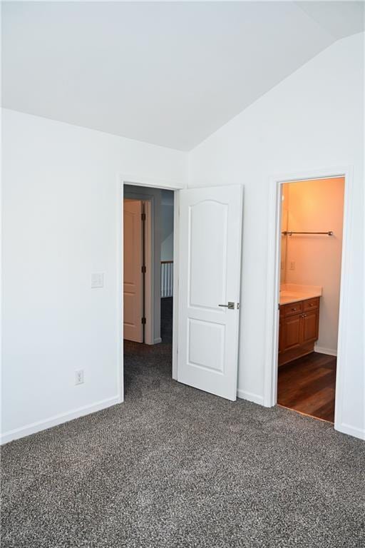 unfurnished bedroom featuring lofted ceiling, ensuite bathroom, and dark carpet