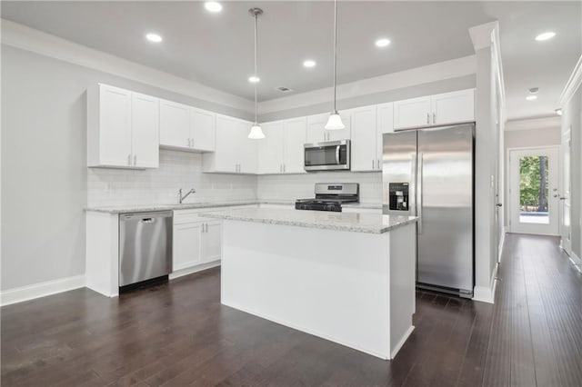 kitchen with appliances with stainless steel finishes, white cabinetry, hanging light fixtures, backsplash, and a kitchen island