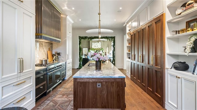 interior space with an island with sink, pendant lighting, white cabinets, and double oven range