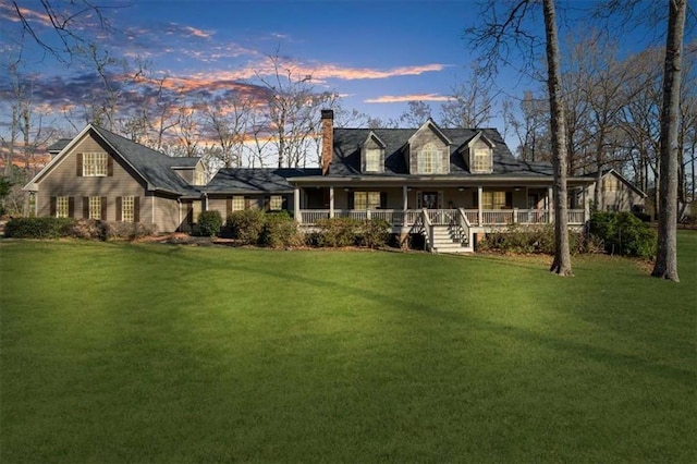 back house at dusk featuring a porch and a lawn