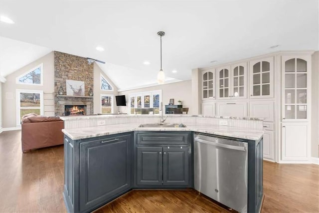 kitchen with a center island with sink, light stone counters, stainless steel dishwasher, decorative light fixtures, and sink