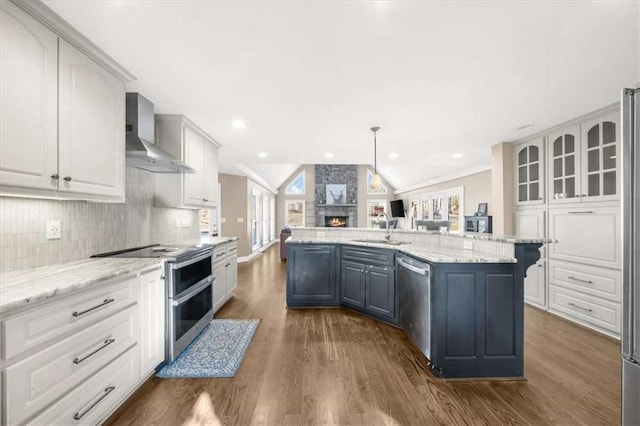 kitchen with wall chimney exhaust hood, stainless steel appliances, lofted ceiling, pendant lighting, and a kitchen island with sink