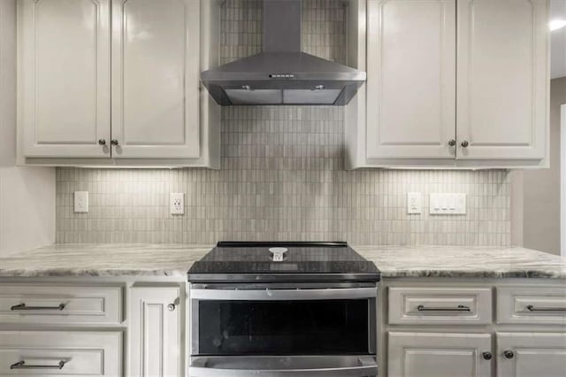 kitchen with light stone counters, wall chimney exhaust hood, white cabinets, stainless steel electric range, and tasteful backsplash