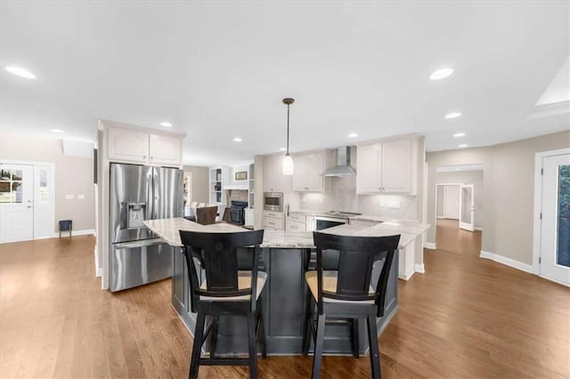 kitchen with appliances with stainless steel finishes, wall chimney exhaust hood, white cabinets, pendant lighting, and a kitchen island