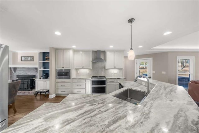 kitchen featuring appliances with stainless steel finishes, sink, decorative light fixtures, wall chimney exhaust hood, and light stone countertops