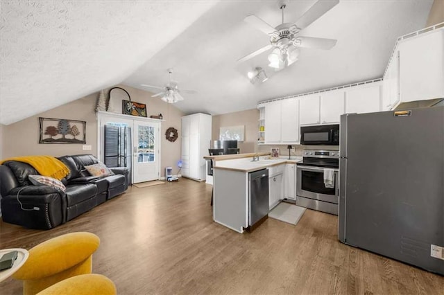 kitchen featuring appliances with stainless steel finishes, wood-type flooring, vaulted ceiling, white cabinetry, and kitchen peninsula