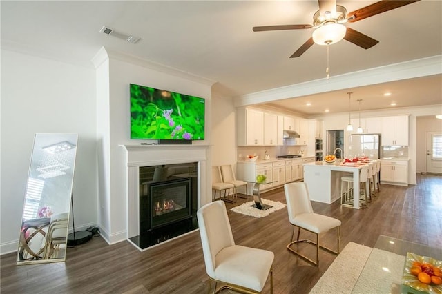 living area featuring dark wood-type flooring, a glass covered fireplace, visible vents, and crown molding