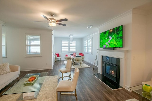 living area with dark wood-type flooring, a glass covered fireplace, and crown molding