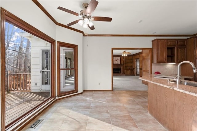 kitchen featuring sink, backsplash, light stone counters, ceiling fan, and ornamental molding