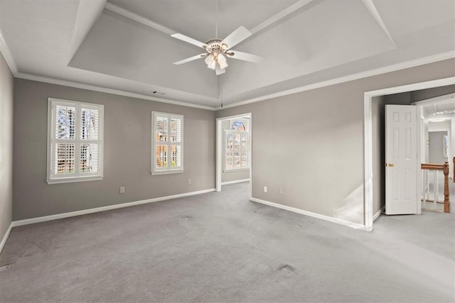 empty room with ceiling fan, a tray ceiling, carpet floors, and ornamental molding