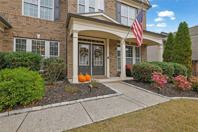 view of exterior entry featuring brick siding and a porch