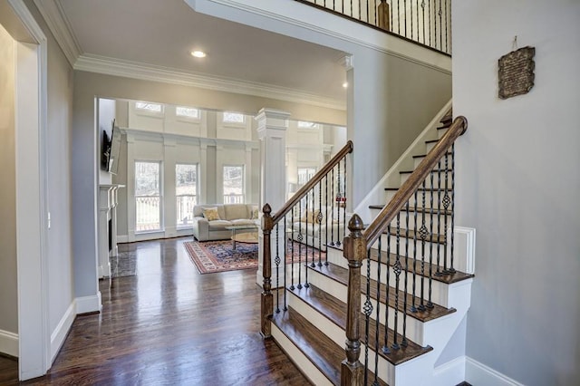 stairway featuring baseboards, ornamental molding, a fireplace, wood finished floors, and ornate columns